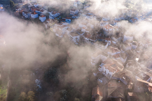 Aerial view of the historic village of Avo shrouded in thick morning fog with red tiled rooftops peeking through the mist in Oliveira do Hospital Coimbra District Portugal.