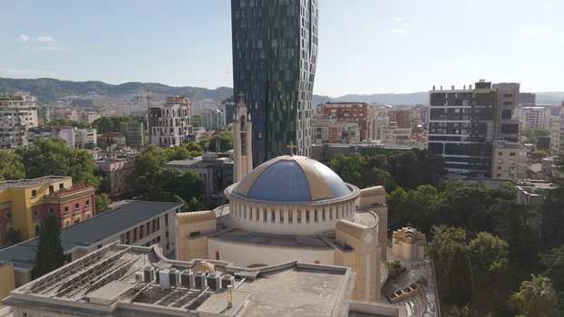 Aerial view of the Orthodox Cathedral of Resurrection with its distinctive blue dome surrounded by modern high rise buildings and lush green trees in Tirane Qarku i Tiranes Albania.