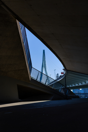 View of the Erasmus Bridge pylon through a geometric concrete opening with sharp shadows and clear blue sky in Rotterdam South Holland Netherlands. View of the Erasmus Bridge pylon through a geometric concrete opening with sharp shadows and clear blue sky in Rotterdam South Holland Netherlands.