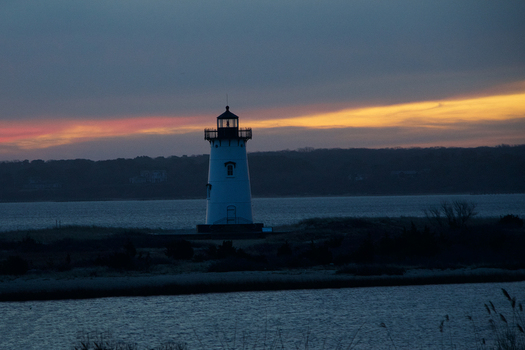 View of the Edgartown Harbor Light at sunset with vibrant orange and pink clouds over the calm water of Martha s Vineyard Edgartown Massachusetts United States.