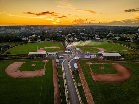 Aerial view of Quality Baseball Academy featuring baseball fields with green grass and dirt infields under a sunset sky in San Antonio de Guerra Santo Domingo Province Dominican Republic. Aerial view of Quality Baseball Academy featuring baseball fields with green grass and dirt infields under a sunset sky in San Antonio de Guerra Santo Domingo Province Dominican Republic.