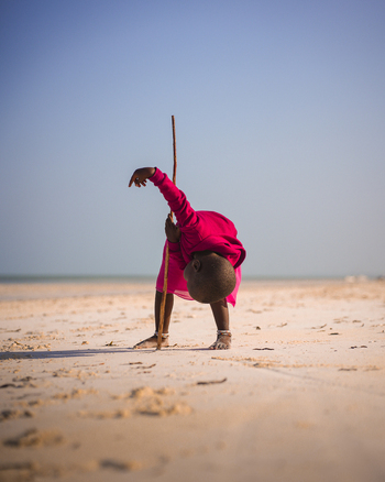 Paje Tanzania 23 January 2025 View of a child in vibrant pink bending low on the sandy beach a slender stick mirroring the curve of their form against the vast serene sky. Paje Tanzania 23 January 2025 View of a child in vibrant pink bending low on the sandy beach a slender stick mirroring the curve of their form against the vast serene sky.