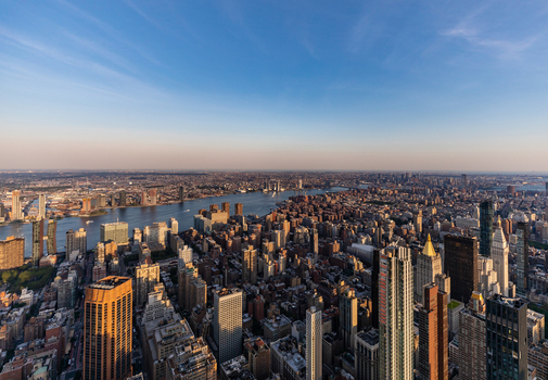 New York United States 09 August 2021 Aerial view of the dense Manhattan skyline at sunset with the East River flowing between skyscrapers under a clear blue sky.