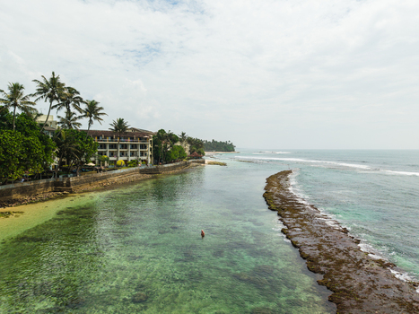 Aerial view of Thalpe Beach featuring a natural rock pool in turquoise water surrounded by palm trees and a coastal resort in Talpe Southern Province Sri Lanka. Aerial view of Thalpe Beach featuring a natural rock pool in turquoise water surrounded by palm trees and a coastal resort in Talpe Southern Province Sri Lanka.