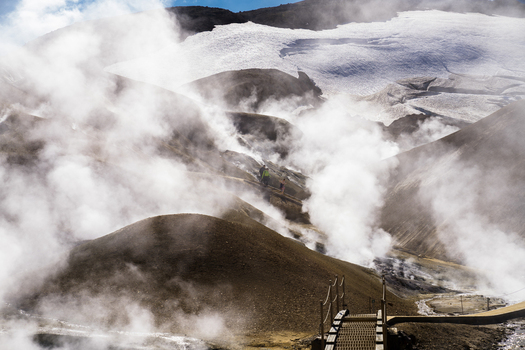 View of geothermal steam rises from the earth against a stark backdrop of snow capped mountains creating a surreal landscape of contrasting elements Hrunamannahreppur Iceland.