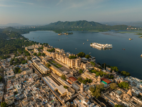 Aerial view of the historic City Palace complex situated on the banks of Lake Pichola featuring intricate architecture courtyards and surrounding urban landscape in Udaipur Rajasthan India.
