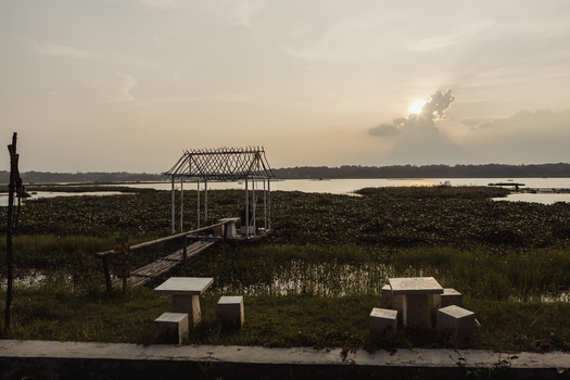 View of a lake covered in water hyacinth with a bamboo gazebo and stone tables at sunset in Kecamatan Tawangmangu Jawa Tengah Indonesia.