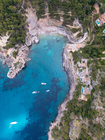 Aerial view of Cala Deia with turquoise water rocky cliffs and boats anchored in the bay in Spain. Aerial view of Cala Deia with turquoise water rocky cliffs and boats anchored in the bay in Spain.