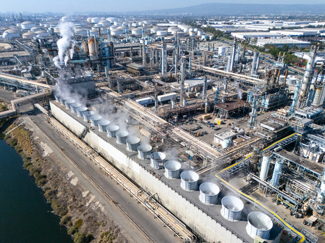 Aerial view of the oil refinery complex with cooling towers industrial pipes and storage tanks under a clear sky in Carson California United States.