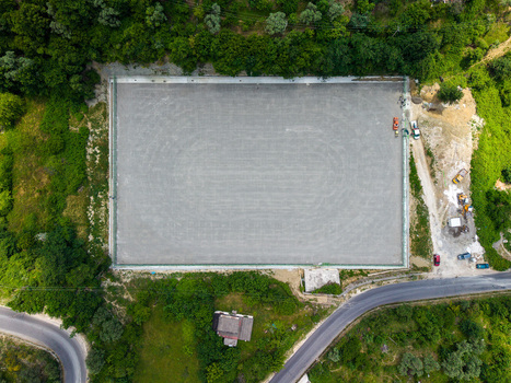 Aerial view of a rectangular construction site surrounded by lush green forest and a winding road in Kruje Durres County Albania.