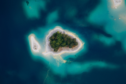 Aerial view of a small island with lush green trees in the turquoise and deep blue waters of Eibsee lake Grainau Bavaria Germany. Aerial view of a small island with lush green trees in the turquoise and deep blue waters of Eibsee lake Grainau Bavaria Germany.
