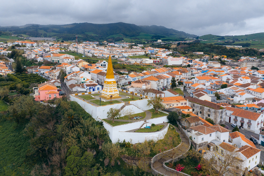 Aerial view of the Alto da Memoria monument overlooking the historic city center with white houses and terracotta roofs under a cloudy sky in Angra do Heroismo Azores Portugal.
