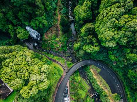 Aerial view of a winding road curving through lush green forests alongside a small stream and waterfall Achada Açores Portugal. Aerial view of a winding road curving through lush green forests alongside a small stream and waterfall Achada Açores Portugal.