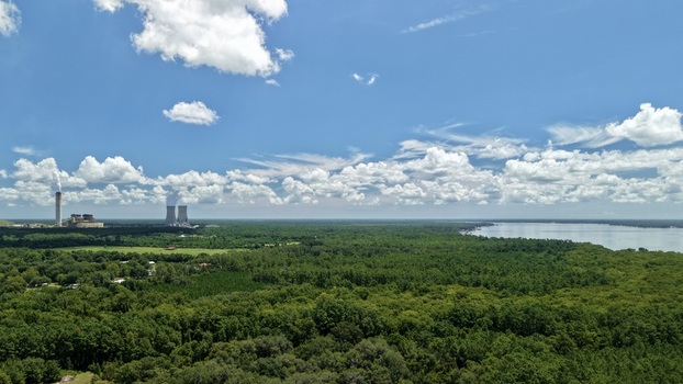 Aerial view of the Seminole Electric power plant with cooling towers and industrial structures set against lush green forest and the St. Johns River in Palatka Florida United States.