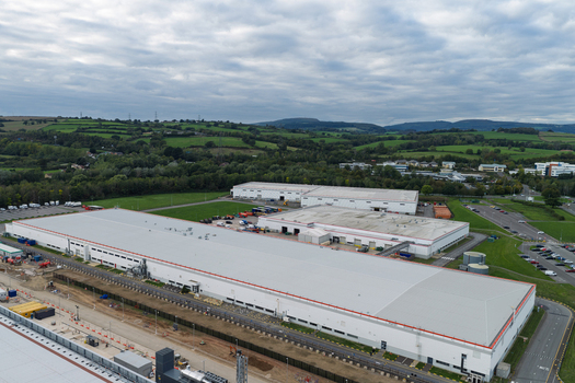 Aerial view of a large data center complex with expansive white rooftops surrounding green fields and paved access roads United Kingdom.