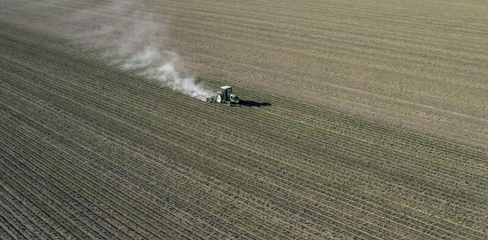 Aerial view of a single tractor working in a vast agricultural field kicking up dust in the bright sunlight Palm Desert California United States. Aerial view of a single tractor working in a vast agricultural field kicking up dust in the bright sunlight Palm Desert California United States.