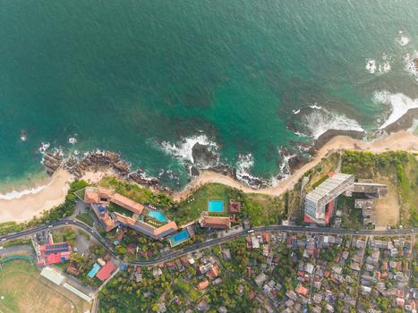 Aerial view of the turquoise coastline featuring luxury resorts with swimming pools rocky shores and urban rooftops along the Indian Ocean in Galle Southern Province Sri Lanka.