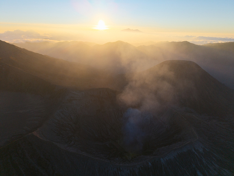 Aerial view of Mount Bromo crater with volcanic smoke rising under a golden sunrise in Tosari East Java Indonesia.