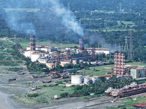 Aerial view of the industrial plant along the Karnaphuli River with smoke rising from stacks storage tanks and cargo ships docked nearby in Chattogram Chattogram Division Bangladesh.
