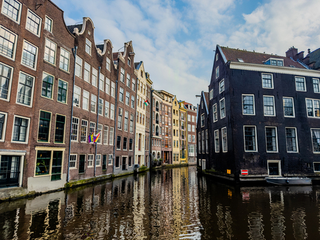 View of traditional gabled canal houses reflecting in the calm water of a canal under a soft blue sky Amsterdam North Holland Netherlands. View of traditional gabled canal houses reflecting in the calm water of a canal under a soft blue sky Amsterdam North Holland Netherlands.
