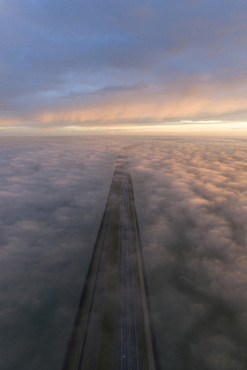 Aerial view of the Afsluitdijk causeway cutting through a dense layer of low clouds and fog under a soft sunset sky in Breezanddijk Friesland Netherlands. Aerial view of the Afsluitdijk causeway cutting through a dense layer of low clouds and fog under a soft sunset sky in Breezanddijk Friesland Netherlands.