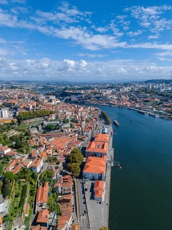 Aerial view of Porto featuring historic buildings with orange rooftops along the Douro River under a blue sky with clouds. Porto Porto District Portugal.