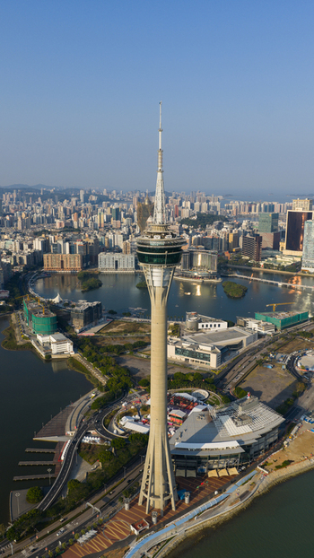 Macao 18 February 2026 Aerial view of the Macau Tower rising above the urban skyline coastal roads and surrounding water under a clear blue sky. Macao 18 February 2026 Aerial view of the Macau Tower rising above the urban skyline coastal roads and surrounding water under a clear blue sky.