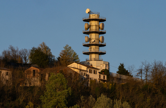 Aerial view of the Television Tower Tortona with its telecommunications antennas and satellite dishes on a hilltop surrounded by trees and houses Tortona Piedmont Italy.
