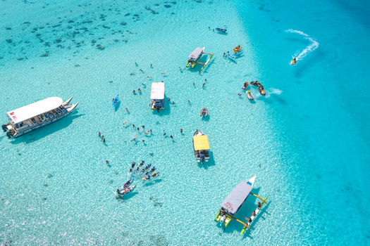 View of a vibrant turquoise lagoon filled with boats and people swimming in the clear shallow water in Moorea Maiao Windward Islands French Polynesia.