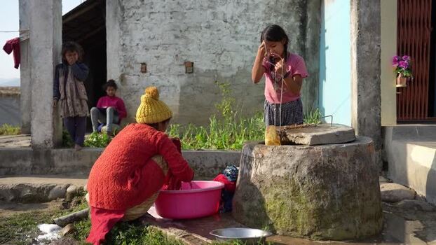 View of women and children washing clothes and face at a well Nepal.