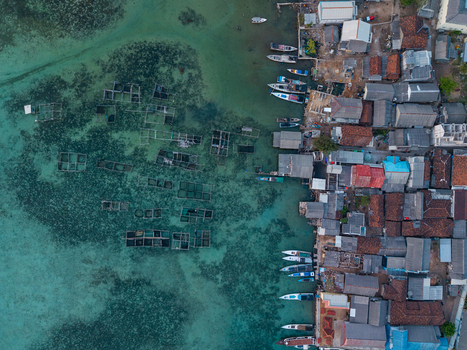 Aerial view of Karimunjawa village with traditional fishing boats moored along the coast and fish farming cages in the clear turquoise water Karimunjawa Central Java Indonesia. Aerial view of Karimunjawa village with traditional fishing boats moored along the coast and fish farming cages in the clear turquoise water Karimunjawa Central Java Indonesia.