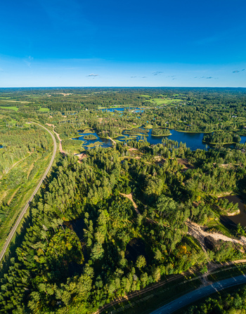 Aerial view of dense forests winding roads and scattered blue lakes under a clear blue sky in Latvia. Aerial view of dense forests winding roads and scattered blue lakes under a clear blue sky in Latvia.