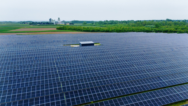 Aerial view of a vast solar panel farm surrounded by green agricultural fields and industrial buildings under an overcast sky in Sabac Vojvodina Serbia.