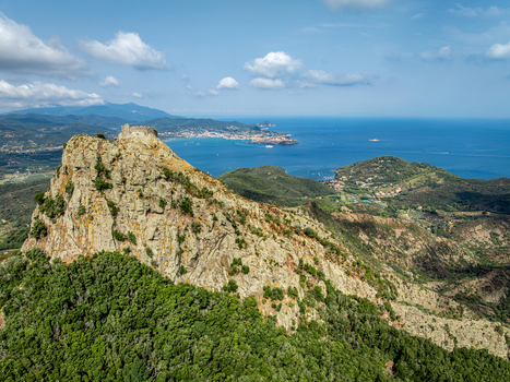 Aerial view of Castello del Volterraio perched on a rocky mountain peak overlooking the sea and the town of Portoferraio surrounded by lush green hills in Portoferraio Toscana Italy.