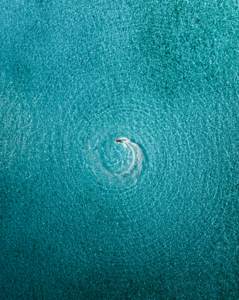 Aerial view of a boat sailing through the crystal clear turquoise waters leaving a swirling wake in its path Noumea New Caledonia. Aerial view of a boat sailing through the crystal clear turquoise waters leaving a swirling wake in its path Noumea New Caledonia.