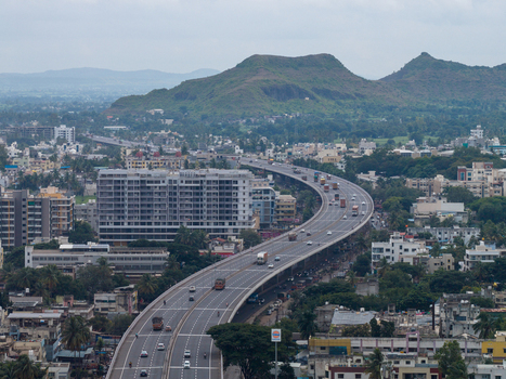 Aerial view of a modern highway flyover winding through the urban landscape of Karad with multi story buildings lush trees and distant hills. Karad Maharashtra India.