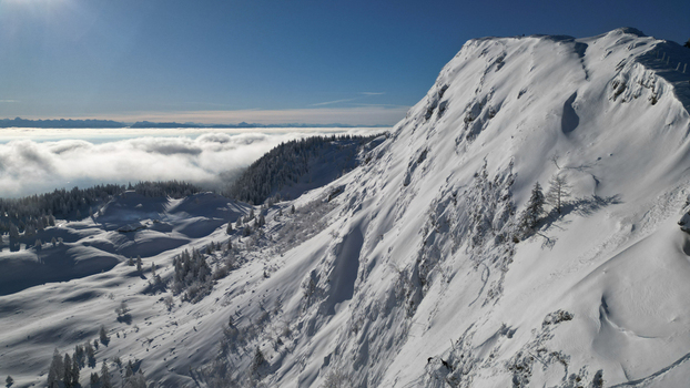 Aerial view of a snow covered mountain peak piercing through a sea of clouds under a crisp blue sky Gingins Vaud Switzerland.