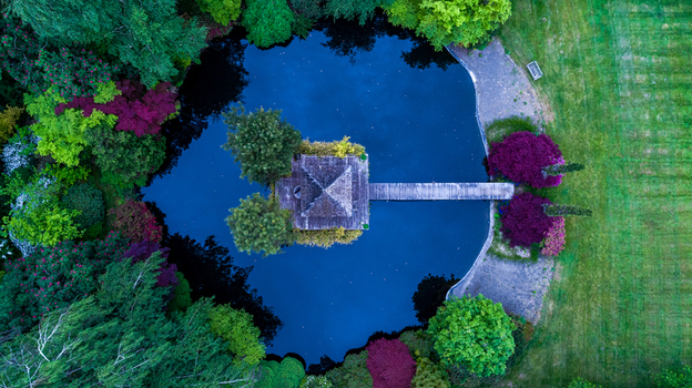 Aerial view of a circular pond with a central pavilion and wooden bridge surrounded by vibrant green and purple trees in Portland Oregon United States. Aerial view of a circular pond with a central pavilion and wooden bridge surrounded by vibrant green and purple trees in Portland Oregon United States.