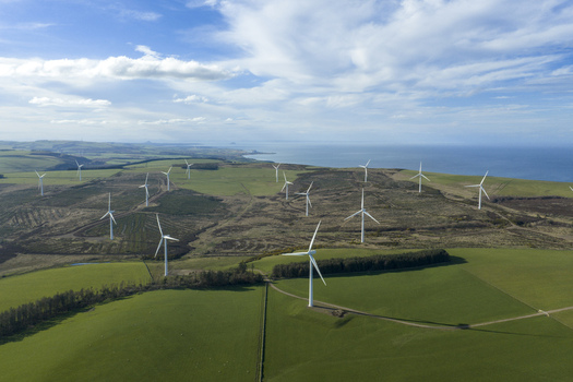 Aerial view of a windfarm with white turbines scattered across rolling green hills under a blue sky with wispy clouds Scotland United Kingdom. Aerial view of a windfarm with white turbines scattered across rolling green hills under a blue sky with wispy clouds Scotland United Kingdom.