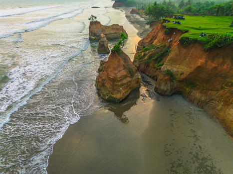 Aerial view of dramatic coastal cliffs and unique rock formations rising from the sandy beach with gentle waves washing the shore in Bali Indonesia. Aerial view of dramatic coastal cliffs and unique rock formations rising from the sandy beach with gentle waves washing the shore in Bali Indonesia.