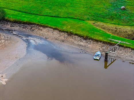 Aerial view of a small boat moored at a riverbank with a wooden pier lush green grass and calm water in Latvia.