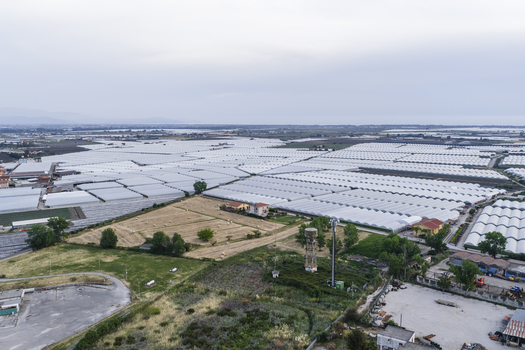 Aerial view of vast agricultural fields with white greenhouses hay bales and a water tower under an overcast sky in Paestum Campania Italy.