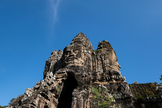 View of the iconic stone faces carved into the towers of Bayon Temple under a clear blue sky in Krong Siem Reap Siem Reap Province Cambodia.
