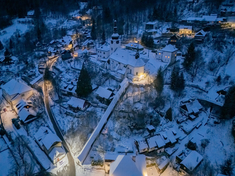 Aerial view of the historic mining village with its illuminated church and snow covered rooftops nestled in a winter forest at dusk Spania Dolina Banska Bystrica Region Slovakia. Aerial view of the historic mining village with its illuminated church and snow covered rooftops nestled in a winter forest at dusk Spania Dolina Banska Bystrica Region Slovakia.