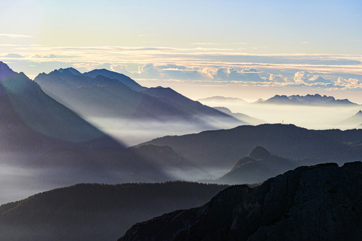 Aerial view of majestic mountains rise through layers of mist their peaks kissed by the soft light of dawn Dolomites of region Friuli as seen from Veneto Italy. Aerial view of majestic mountains rise through layers of mist their peaks kissed by the soft light of dawn Dolomites of region Friuli as seen from Veneto Italy.