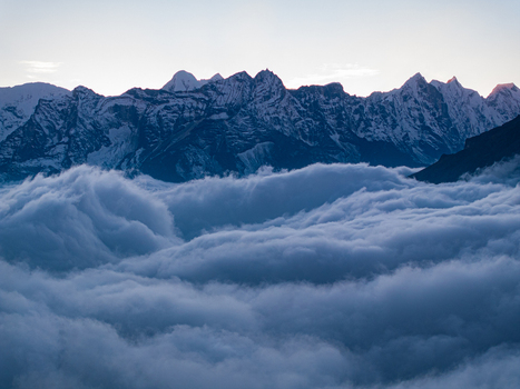 Aerial view of the snow capped Himalayan mountain range rising above a dense sea of clouds at dawn in Nepal.