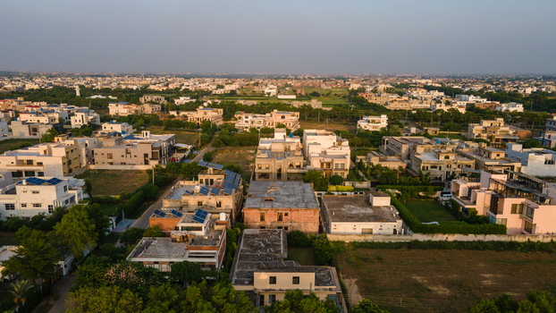 Aerial view of a modern residential neighborhood featuring houses with flat roofs solar panels and surrounding greenery in Lahore Punjab Pakistan.