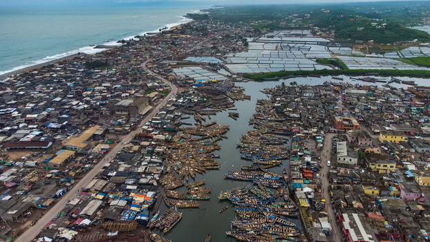 Aerial view of Elmina showing the dense coastal town with numerous fishing boats docked in the lagoon salt pans and the Atlantic Ocean coastline in Elmina Central Region Ghana. Aerial view of Elmina showing the dense coastal town with numerous fishing boats docked in the lagoon salt pans and the Atlantic Ocean coastline in Elmina Central Region Ghana.