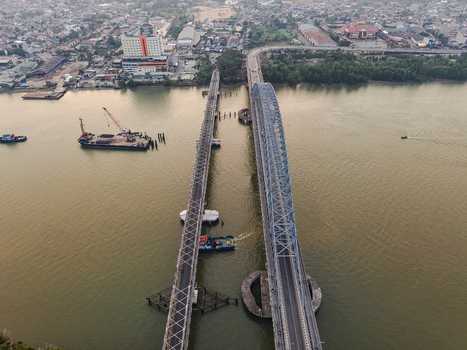 Aerial view of Jembatan Mahakam I spanning the Mahakam River with nearby urban development industrial barges and calm water in Kecamatan Samarinda Seberang Kalimantan Timur Indonesia. Aerial view of Jembatan Mahakam I spanning the Mahakam River with nearby urban development industrial barges and calm water in Kecamatan Samarinda Seberang Kalimantan Timur Indonesia.