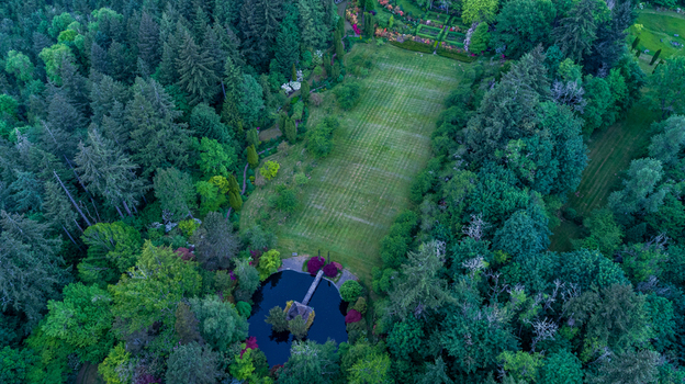 Aerial view of a manicured lawn and a small pond with a gazebo surrounded by a dense evergreen forest in Portland Oregon United States. Aerial view of a manicured lawn and a small pond with a gazebo surrounded by a dense evergreen forest in Portland Oregon United States.